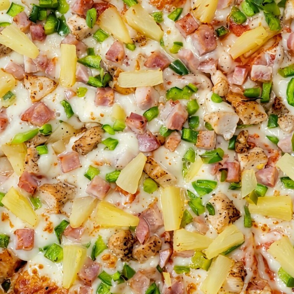 Close-up of a cheesy pizza topped with grilled chicken, ham, pineapple chunks, and green peppers.